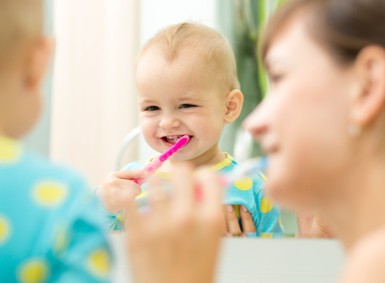 Kind mit Zahnbuerste im Mund vor dem Spiegel