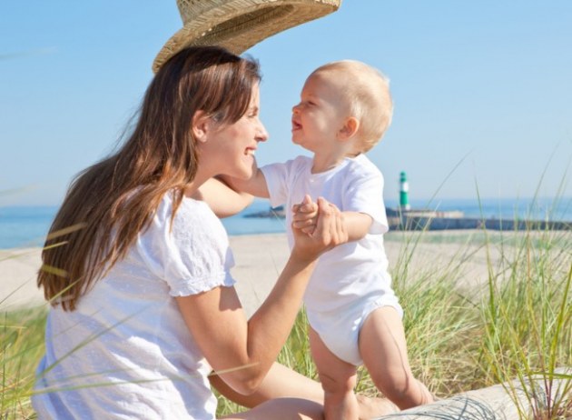 Mama mit Hut und Baby am Strand
