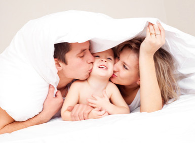 Mama und Papa schmusen mit Kind im Bett
