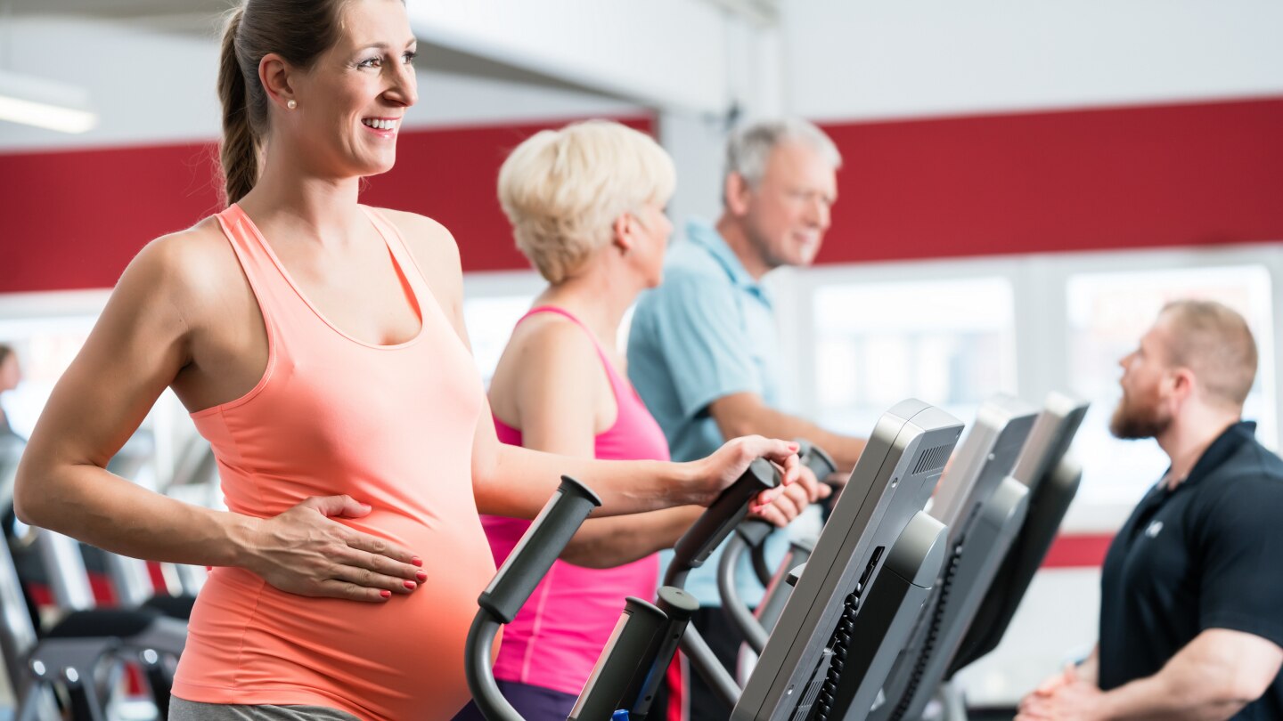 Schwangere Frau und Senioren trainieren am Crosstrainer im Fitnessstudio