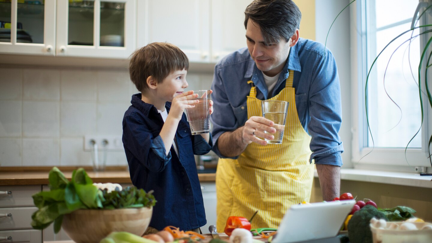Vater und Sohn trinken Glas Wasser beim kochen