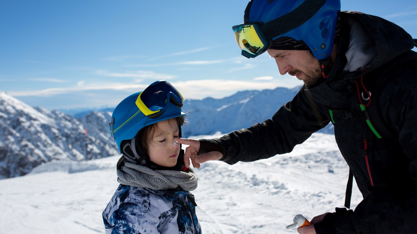 putting sun cream on child's face on top of mountain
