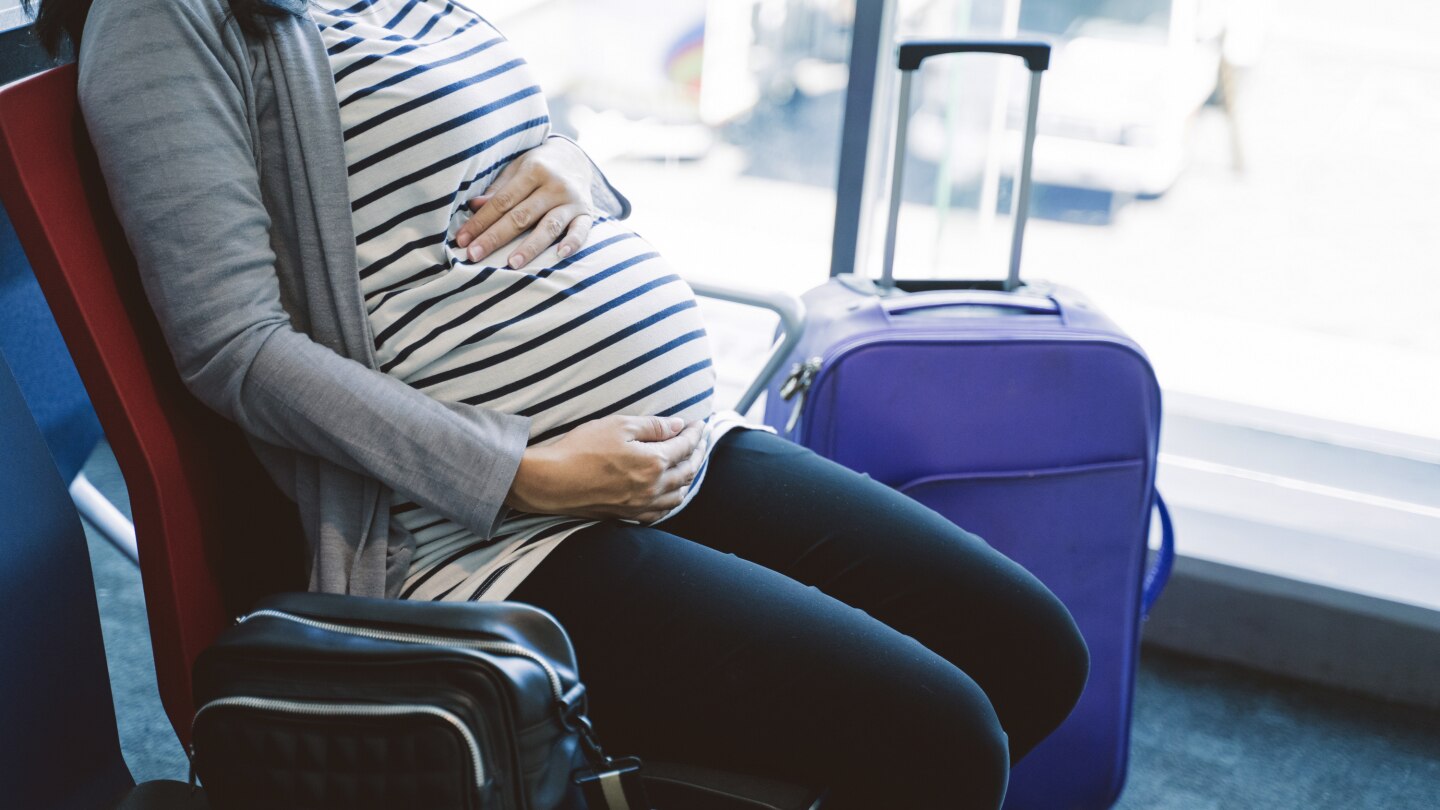 pregnant woman sitting beside a suitcase on the airport