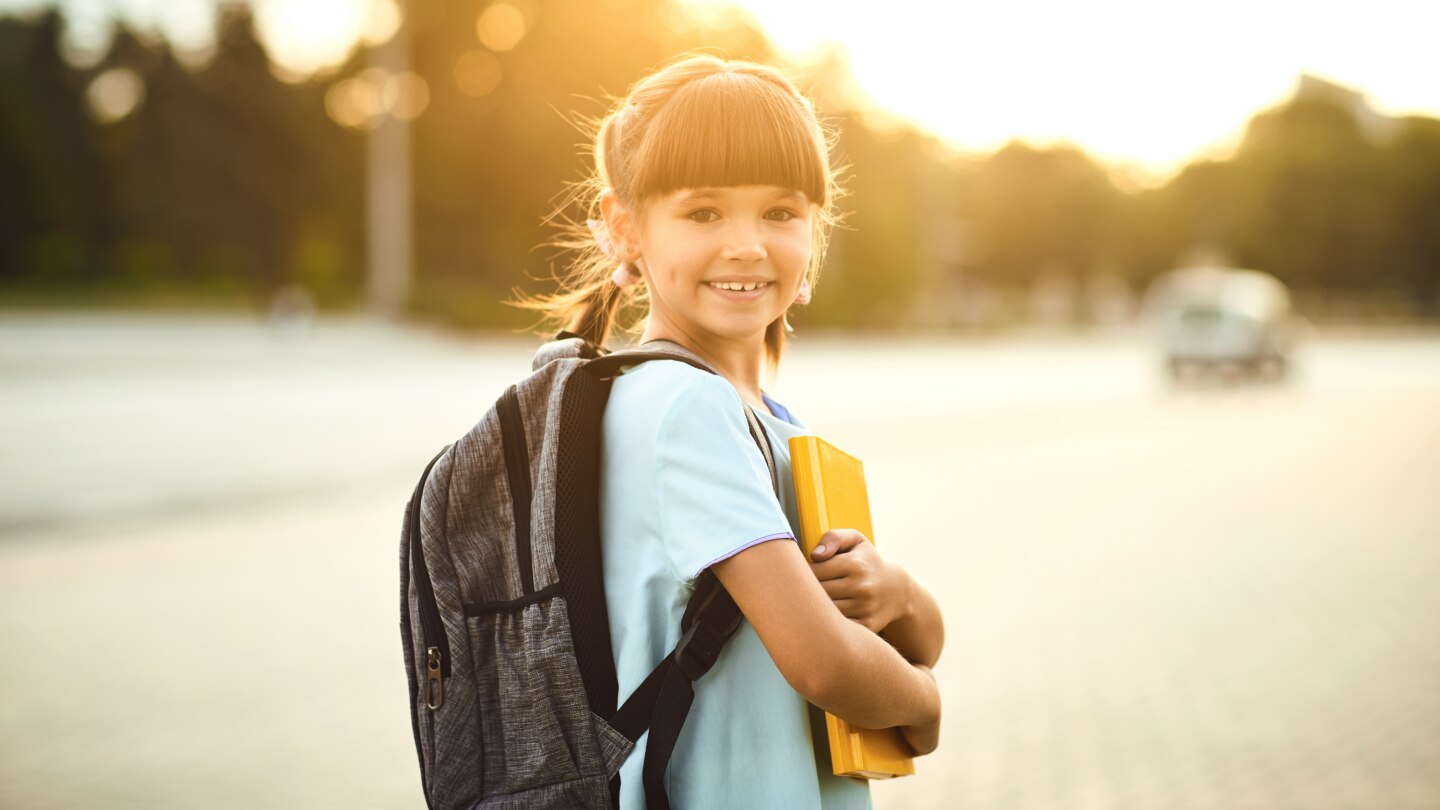 Happy little student girl with a backpack on her way to school