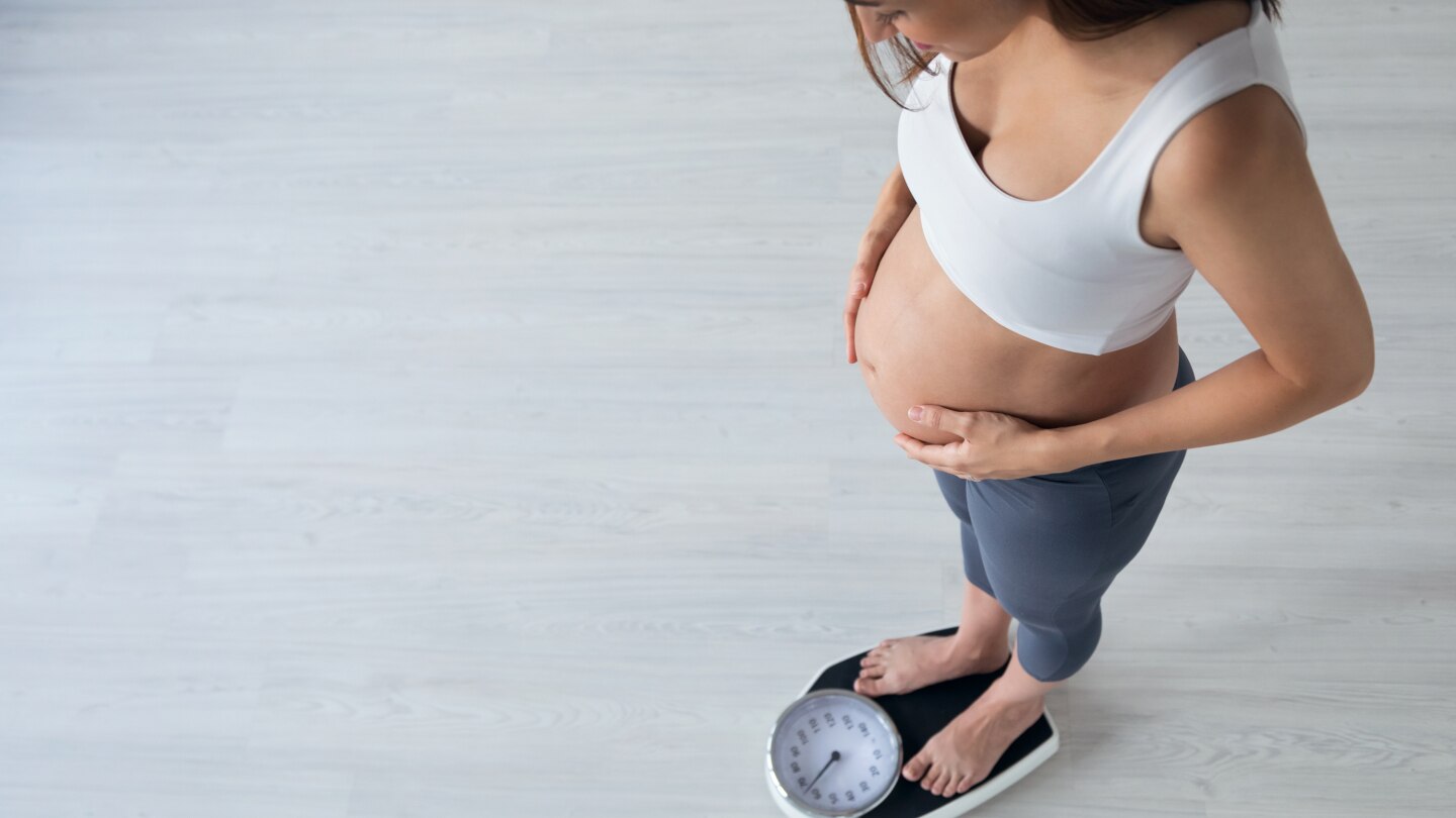 Pretty young pregnant woman standing on scales at home