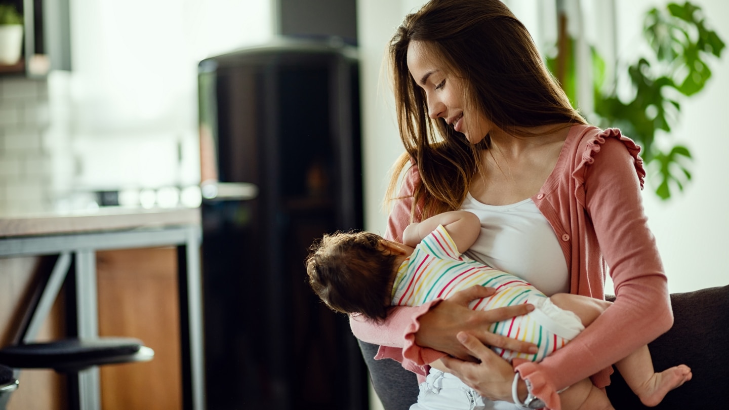 Young smiling mother breastfeeding her baby at home