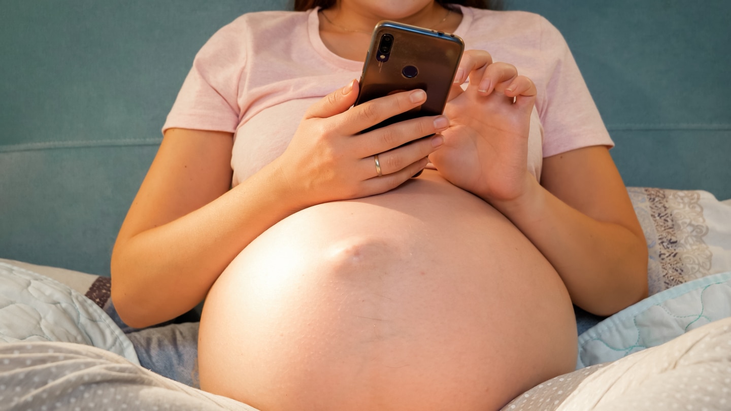Schwangere hält Handy in der Hand