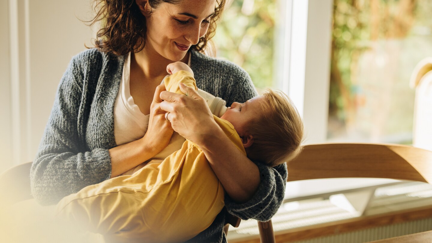 Caring mother feeding milk from bottle to her baby
