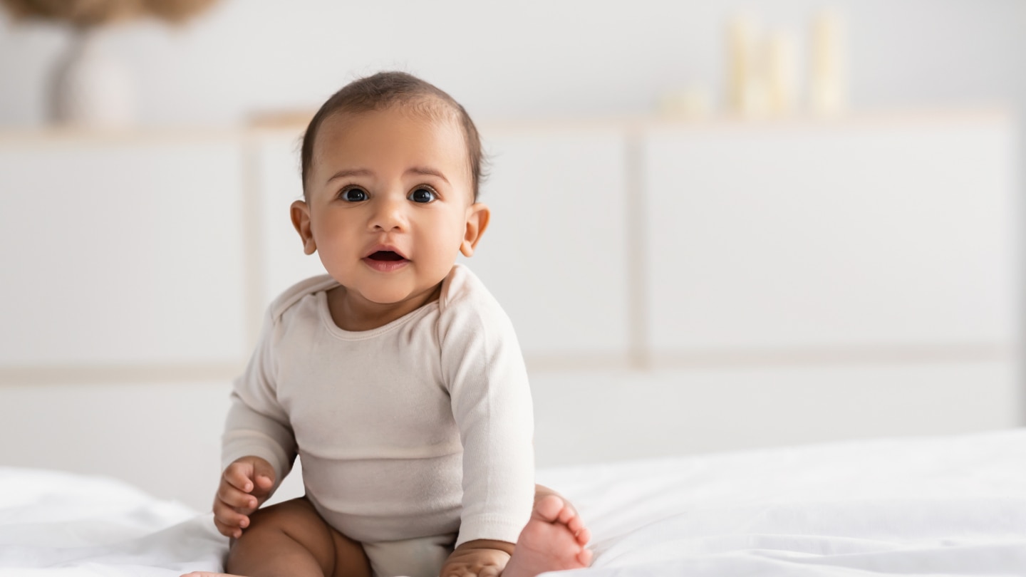 Cute little African American infant sitting on bed