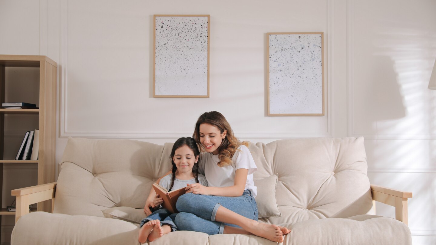 Mother and daughter reading book on sofa at home