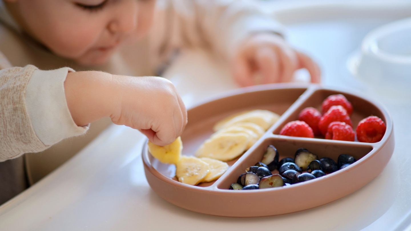 Toddler baby eats fruits and berries with his hand