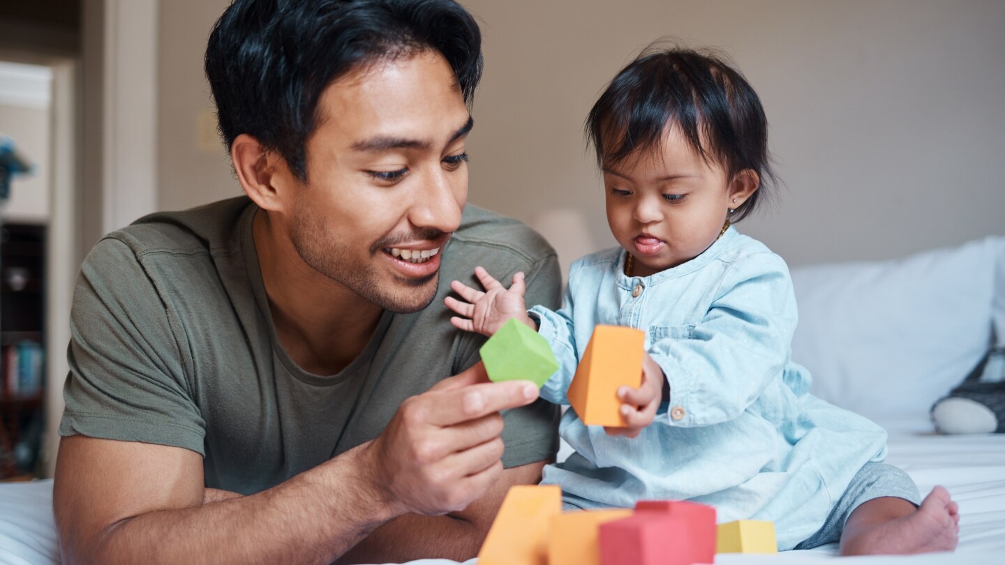Baby, down syndrome and learning on a bed with child and father playing
