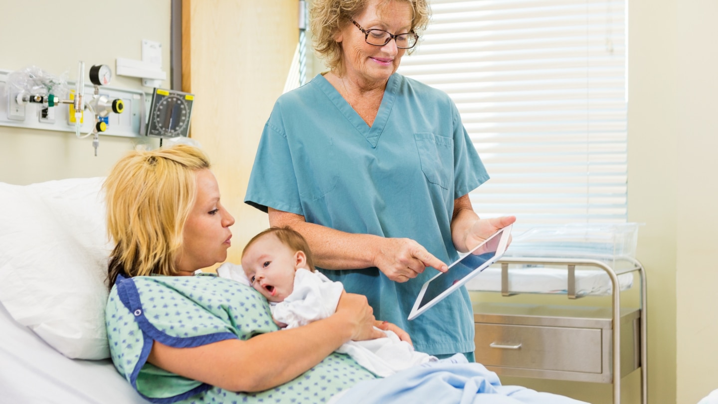 Nurse Explaining Reports On Digital Tablet To Woman With Babygir