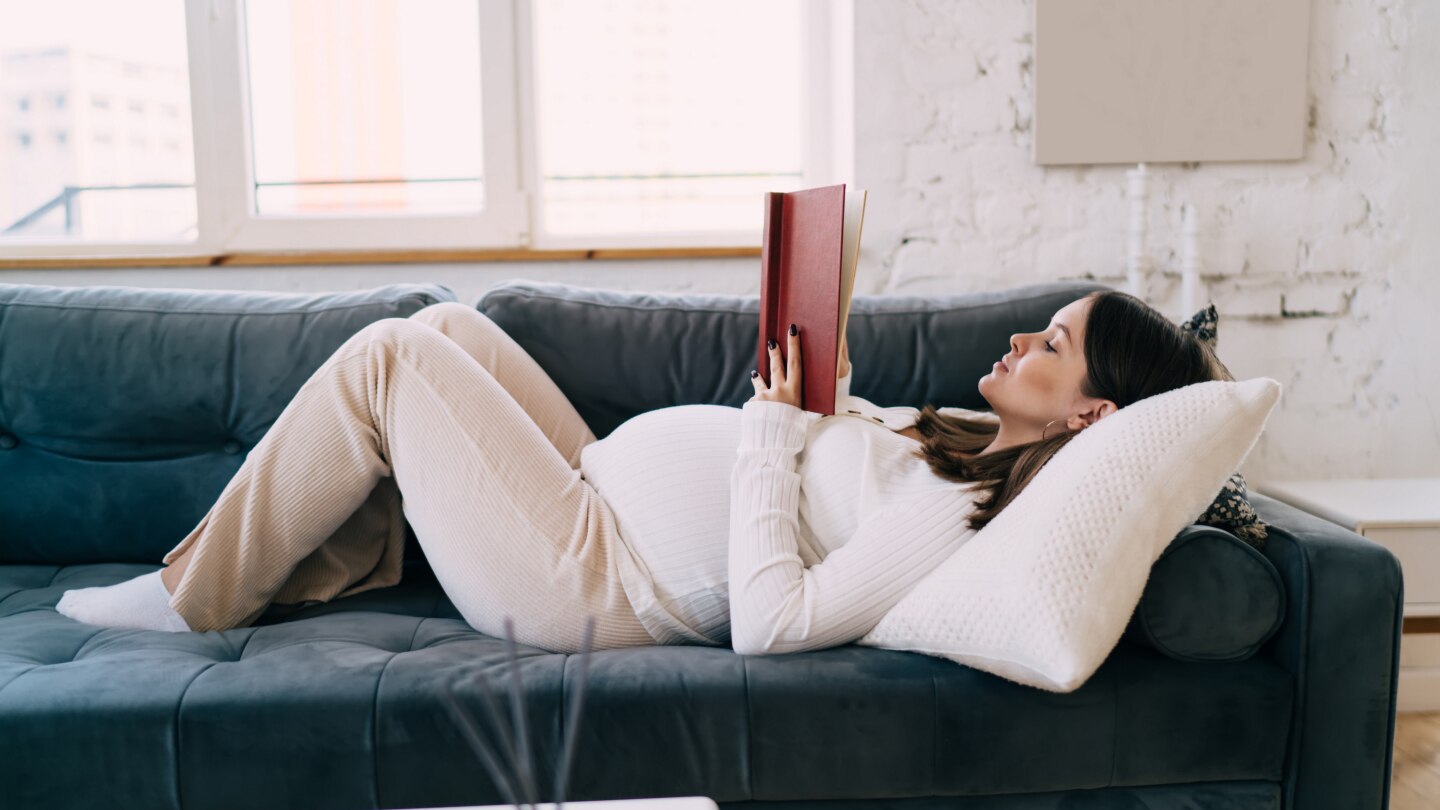 Schwangere liest ein Buch auf der Couch