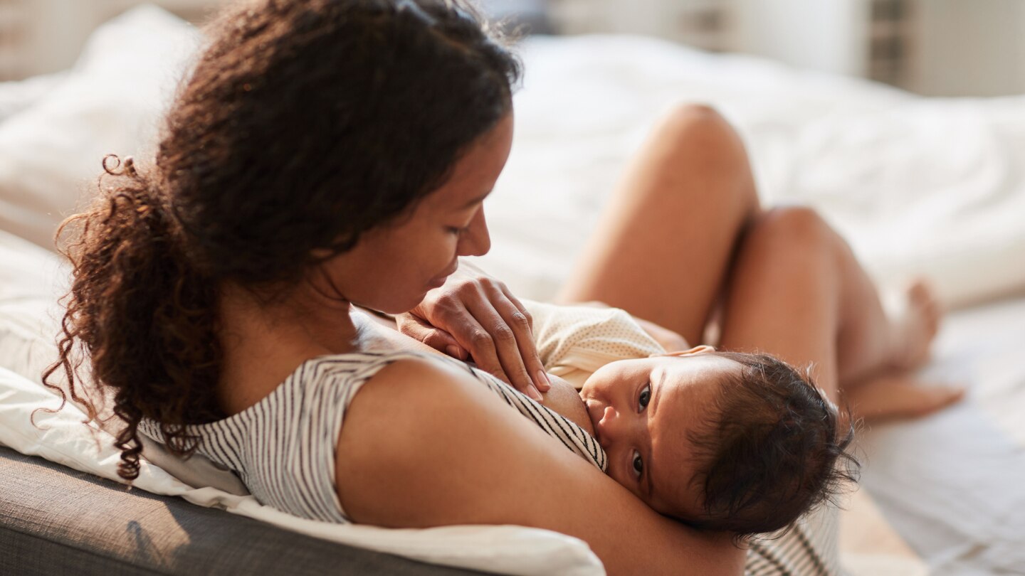 mama sitzt auf dem bett und stillt ihr baby