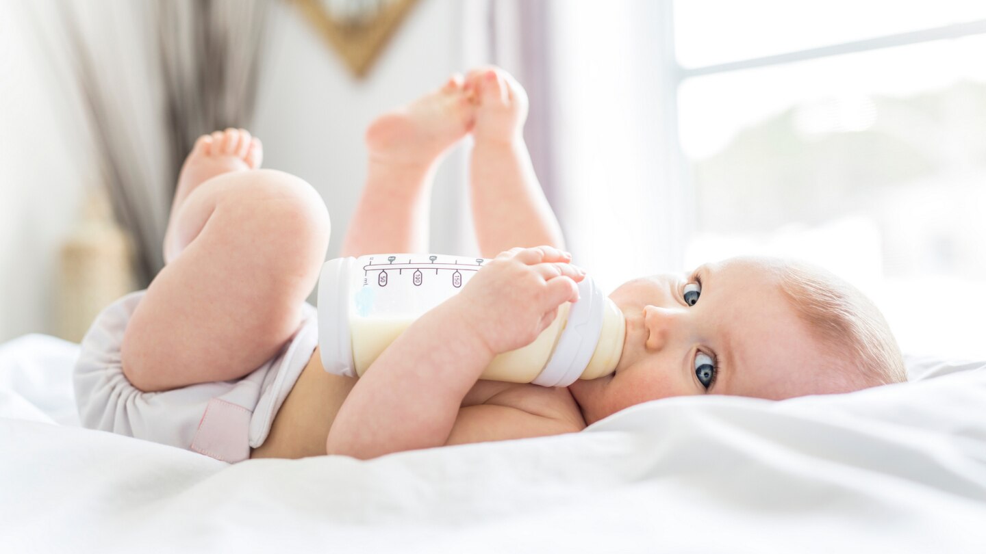baby-liegt-im-bett-und-trinkt-aus-fläschchen
