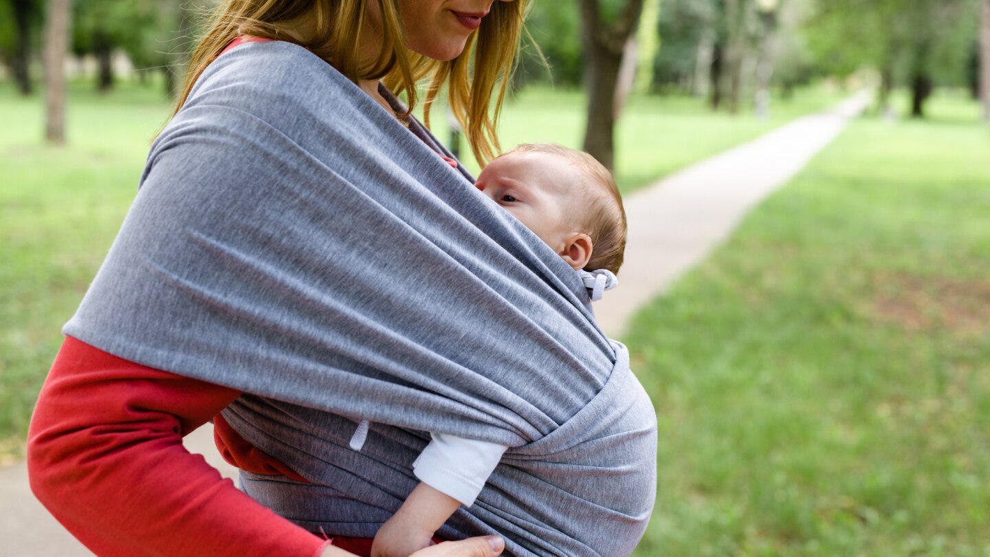 mutter-trägt-baby-mit-tragetuch-im-park