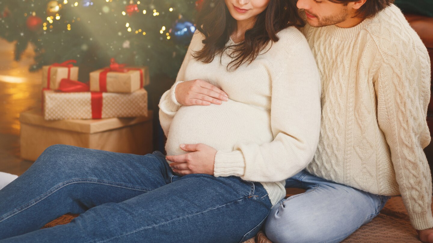 schwangere-und-ihr-partner-vor-einem-weihnachtsbaum-mit-geschenken