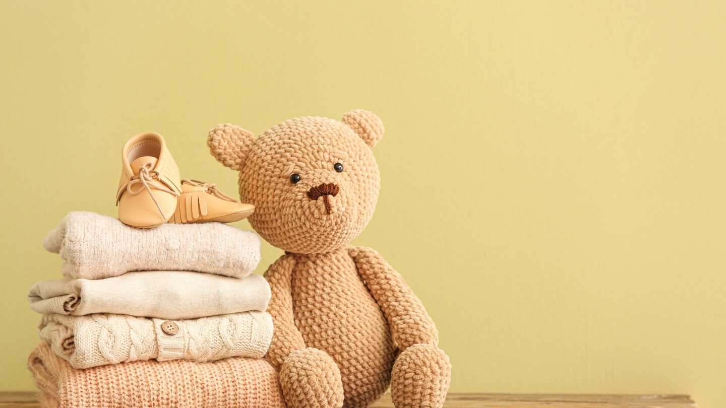 teddybär-neben-stapel-an-babykleidung