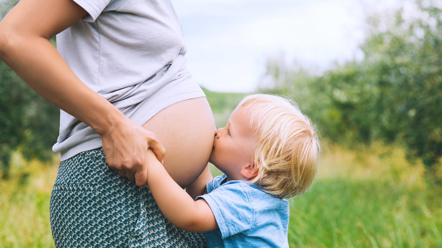 kleinkind kuesst babybauch seiner mama