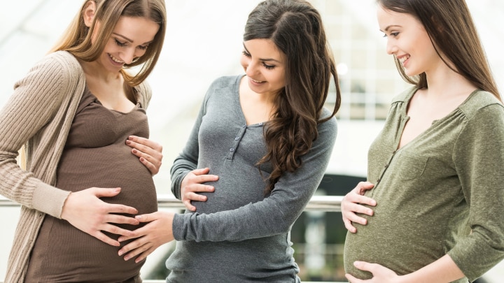 drei schwangere schauen ihre bäuche an
