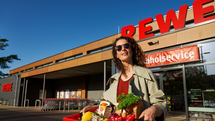 frau vor einem rewe supermarkt