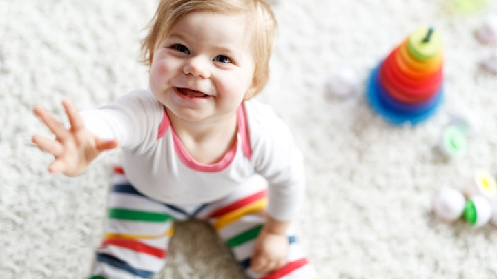 baby sitzt auf dem teppich mit hand nach oben