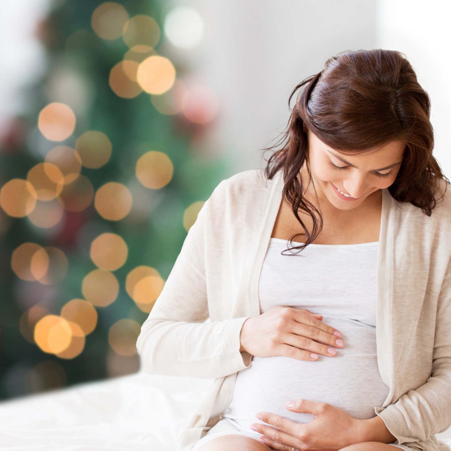 happy pregnant woman sitting on bed at christmas