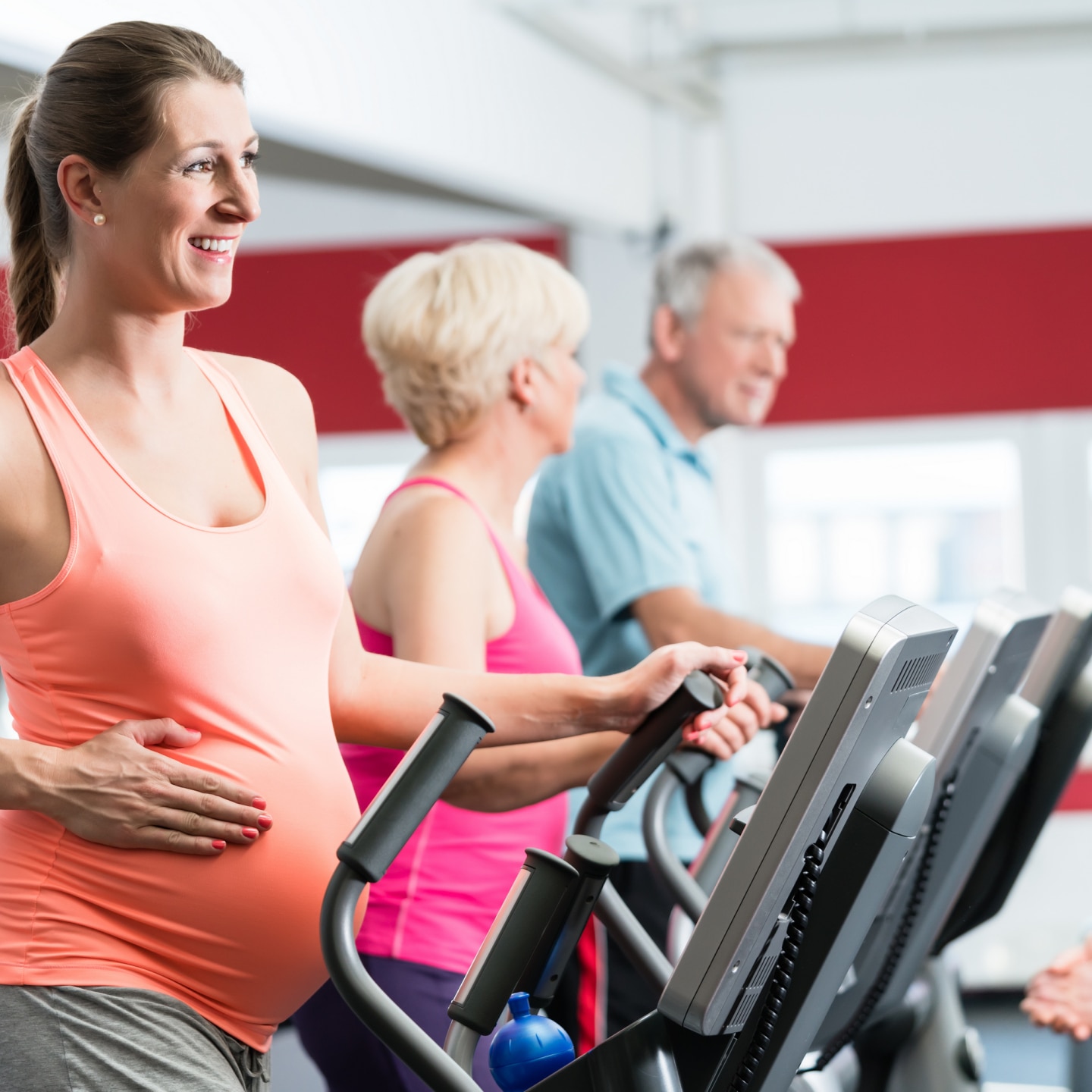 Schwangere Frau und Senioren trainieren am Crosstrainer im Fitnessstudio