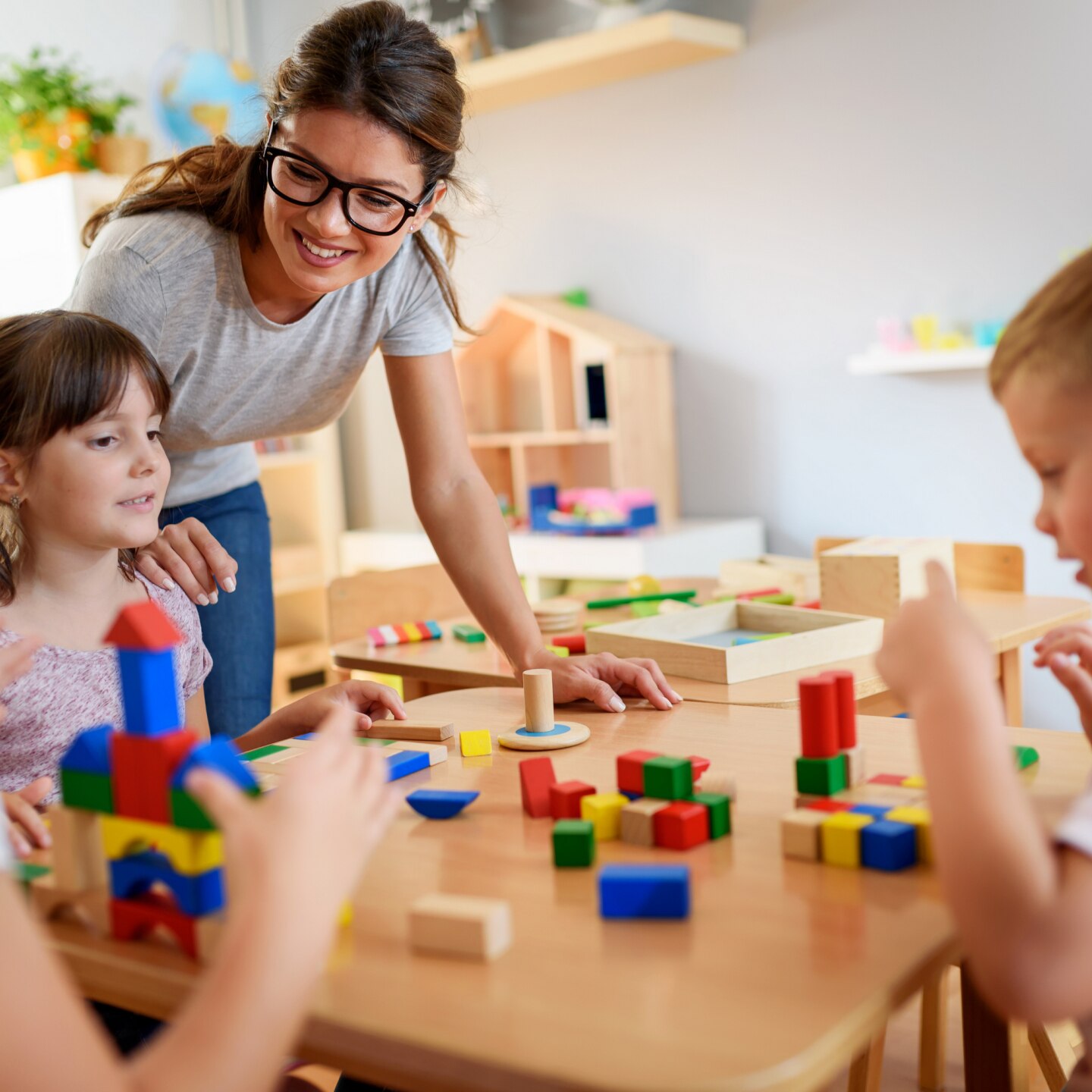 Preschool teacher with children playing with colorful wooden didactic toys at kindergarten