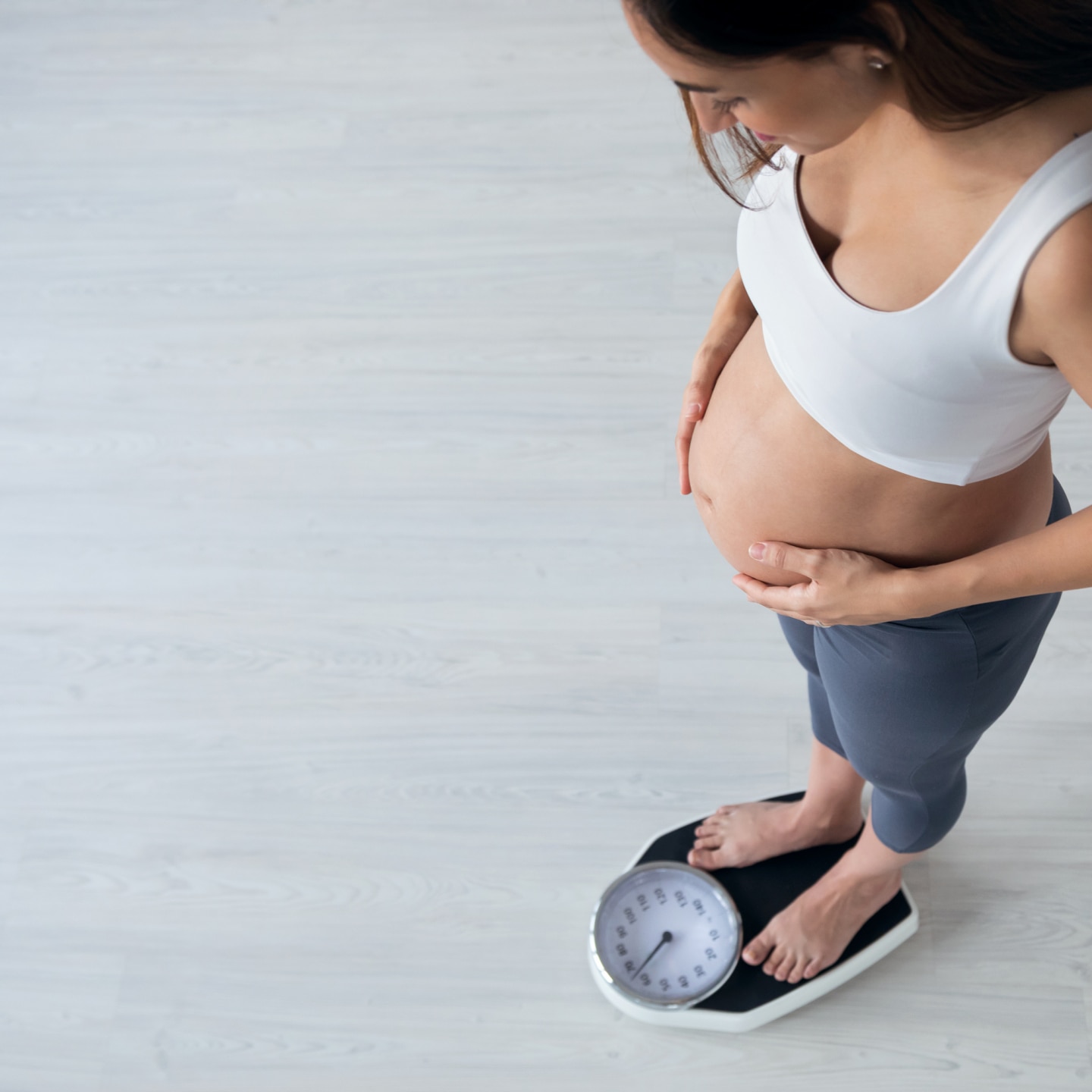 Pretty young pregnant woman standing on scales at home