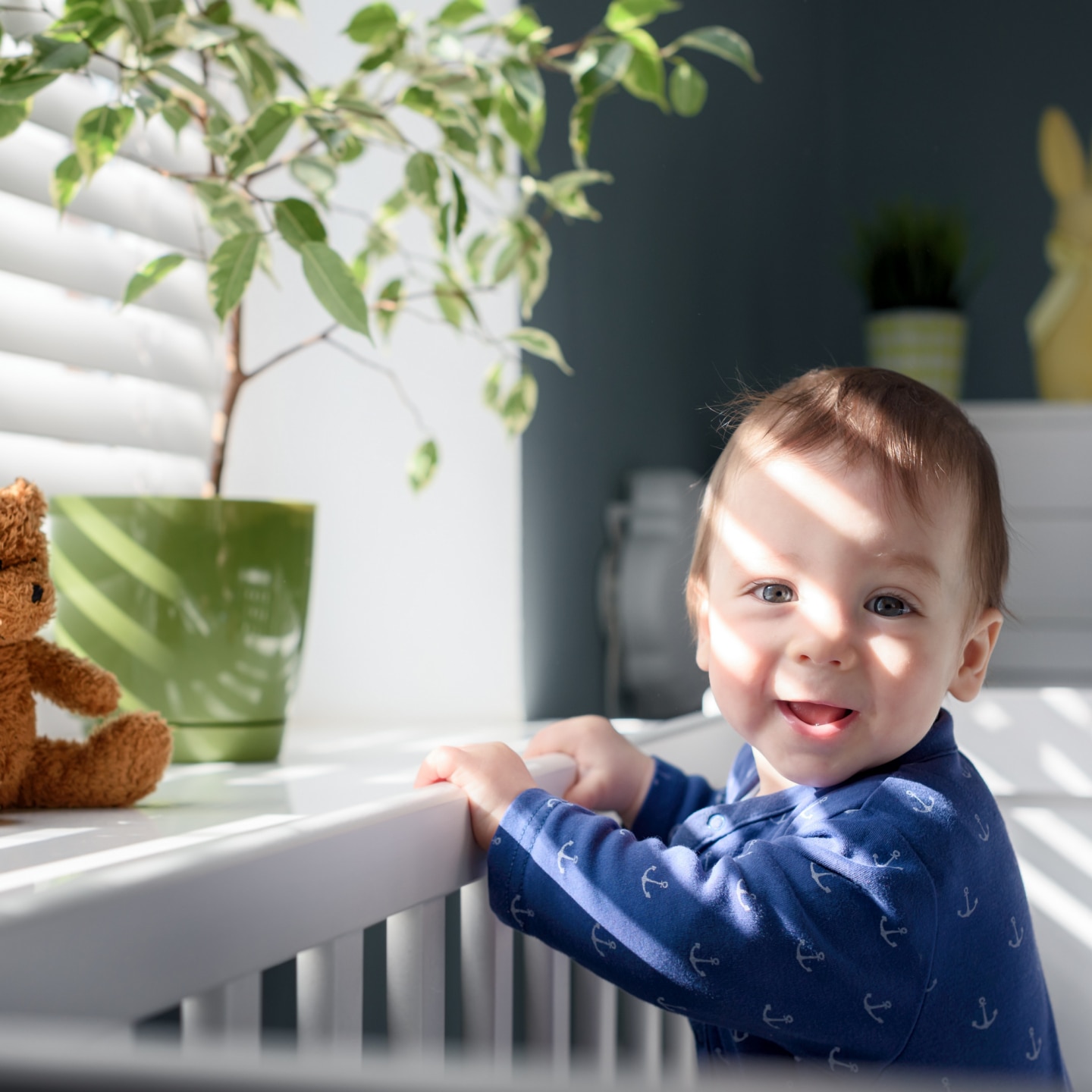 Happy kid near window on white bed in his room