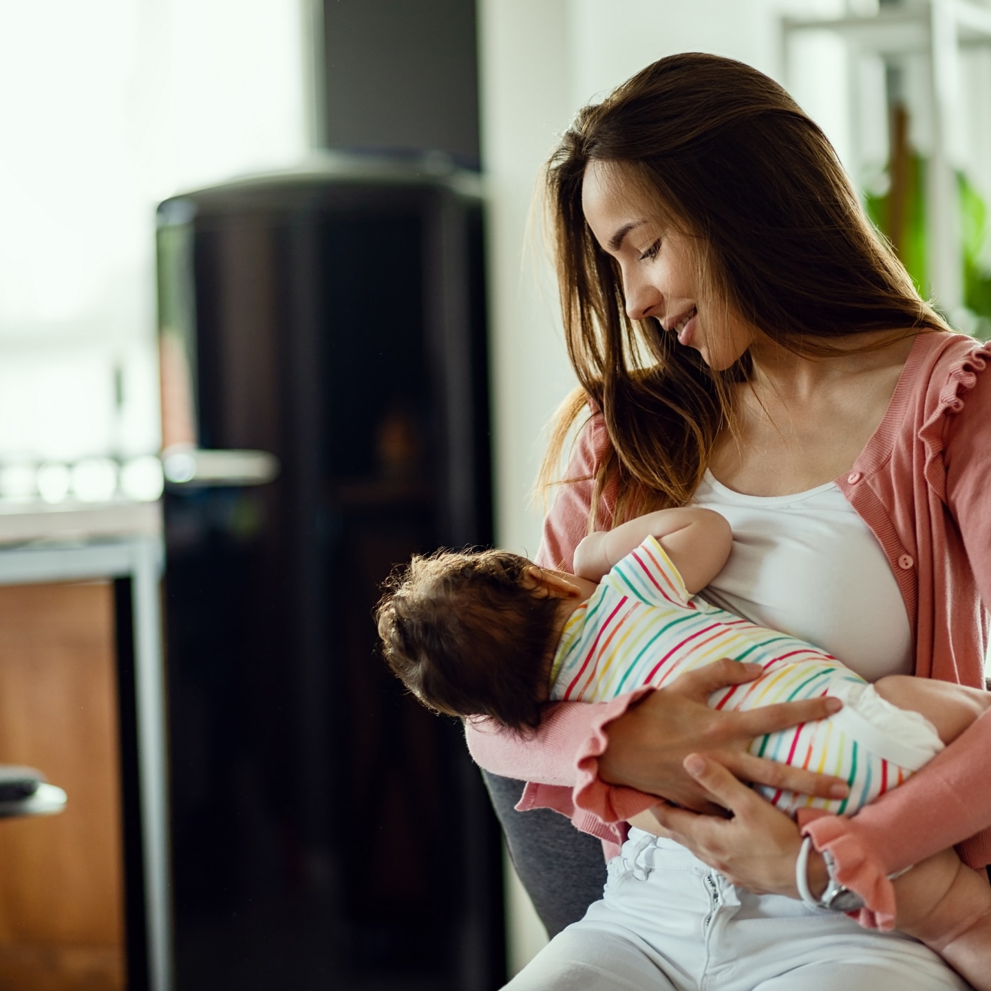 Young smiling mother breastfeeding her baby at home