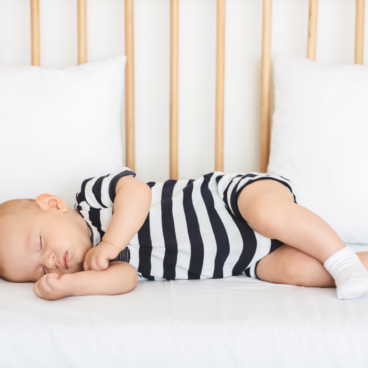 Adorable infant in bodysuit sleeping on his side in bed
