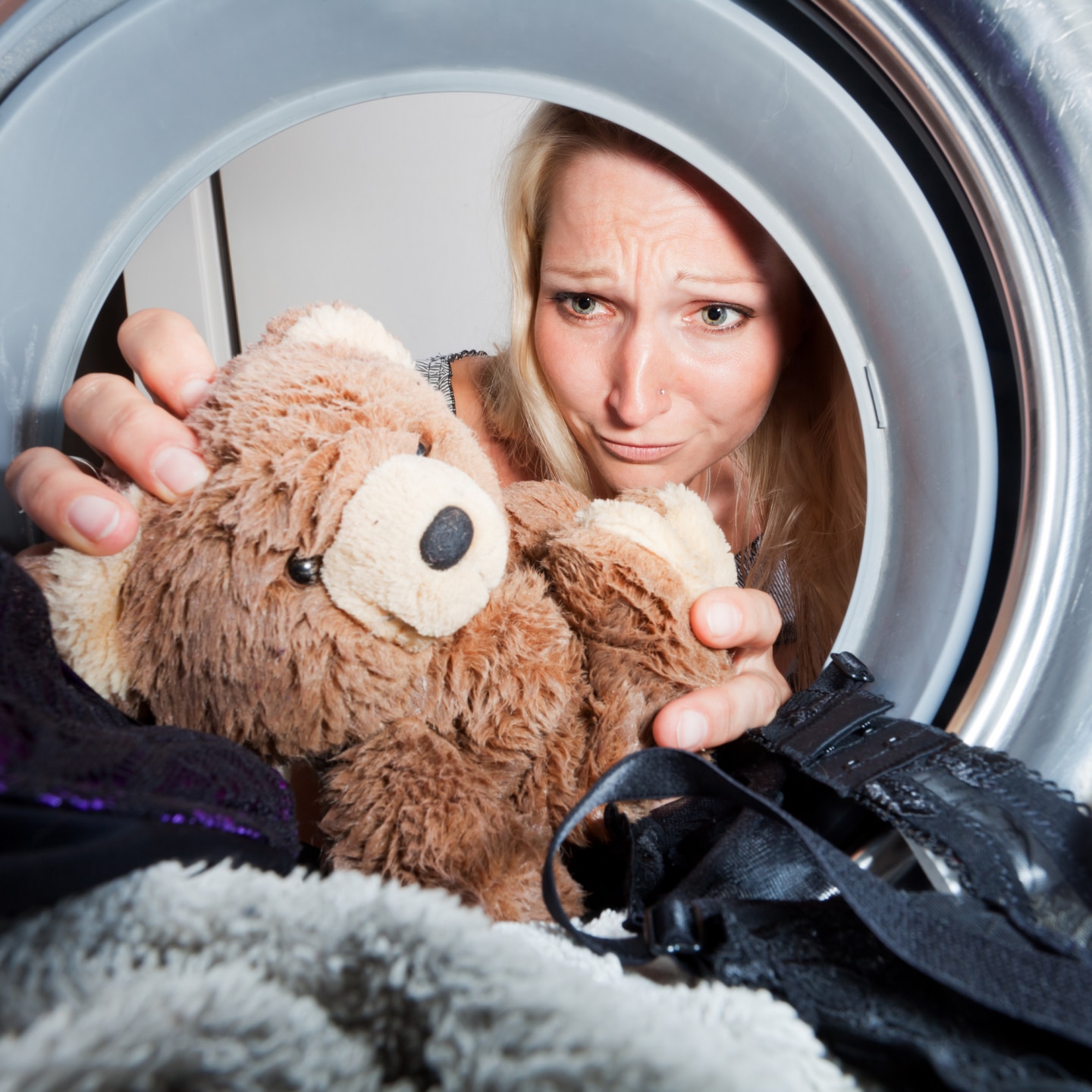 junge Frau holt nassen Teddybär aus einer Waschmaschine