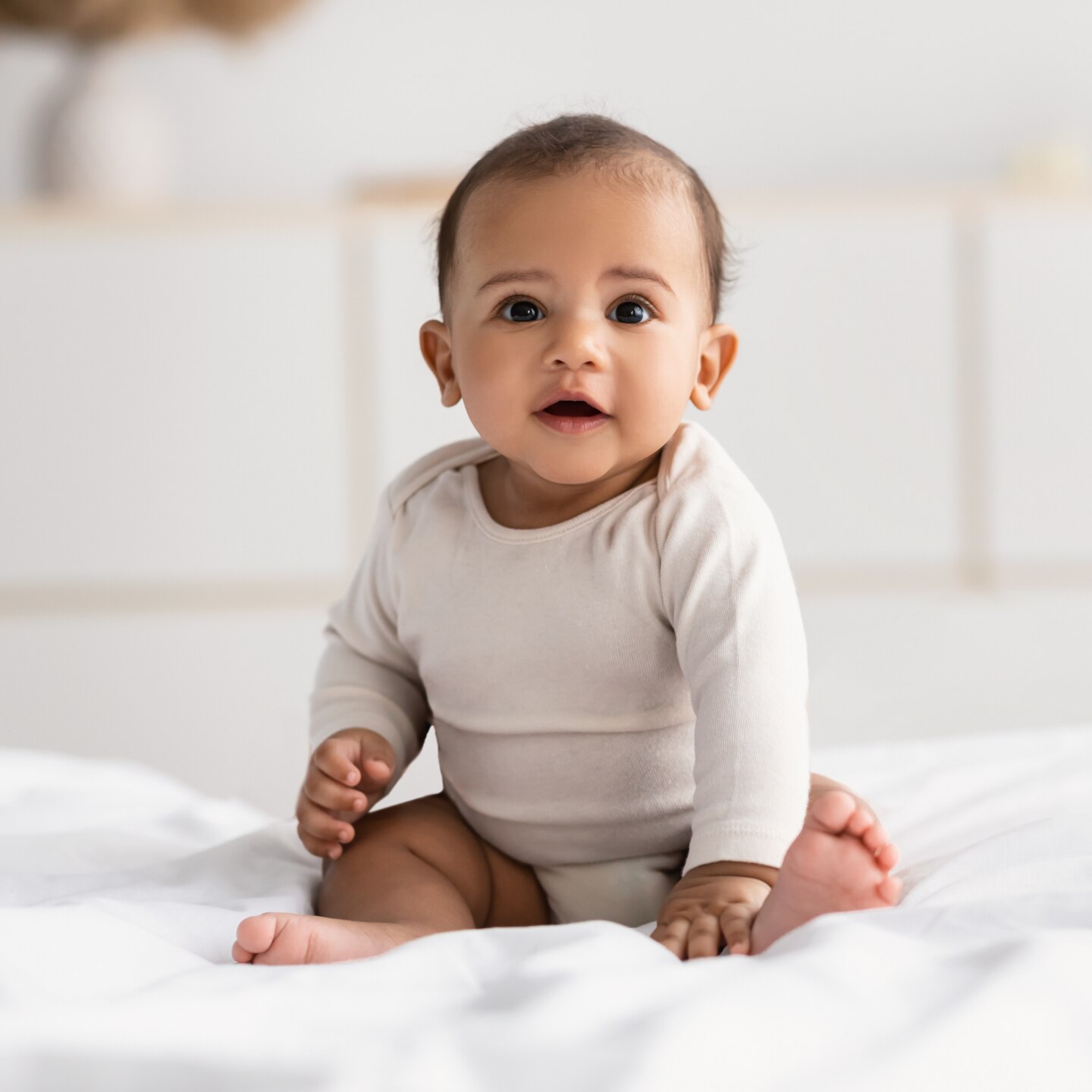Cute little African American infant sitting on bed