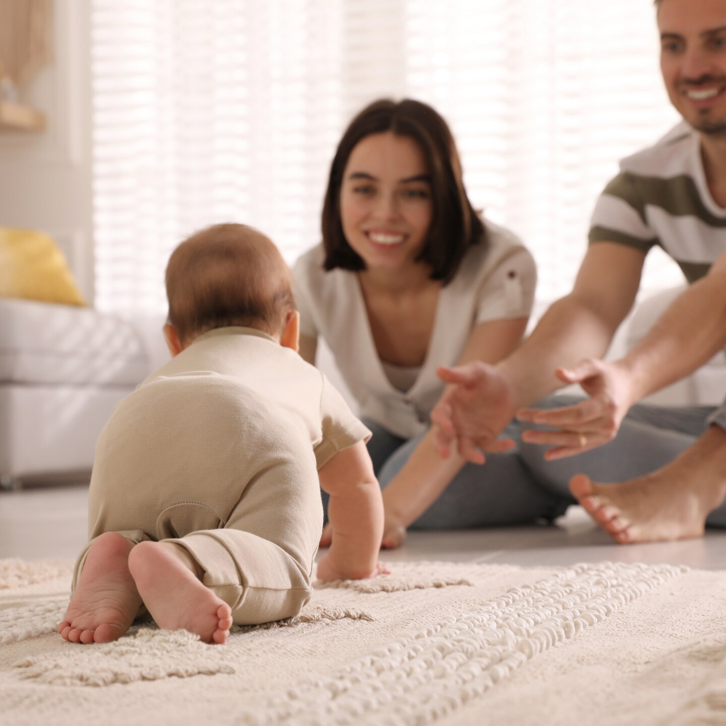 Happy parents watching their cute baby crawl on floor at home