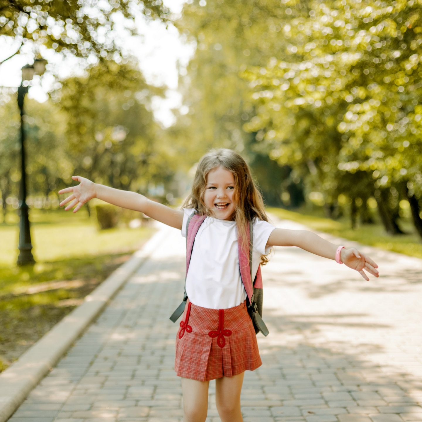 cute schoolgirl with a backpack runs through the park and laughs