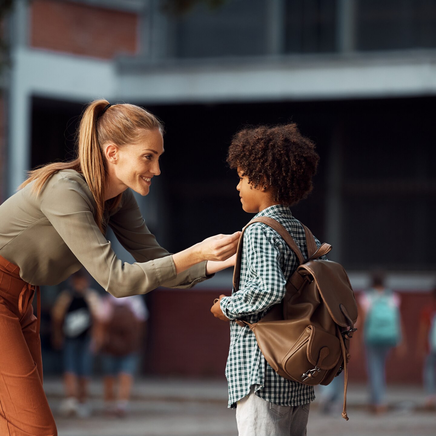 Happy mother greeting with her African American son on first day of school in schoolyard