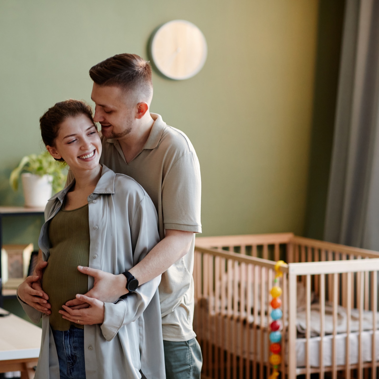 Young man embracing his pregnant wife hile they standing in kids room at home