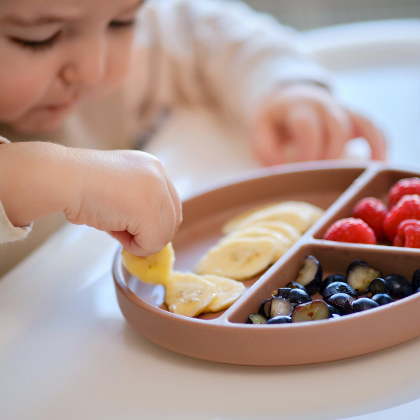 Toddler baby eats fruits and berries with his hand