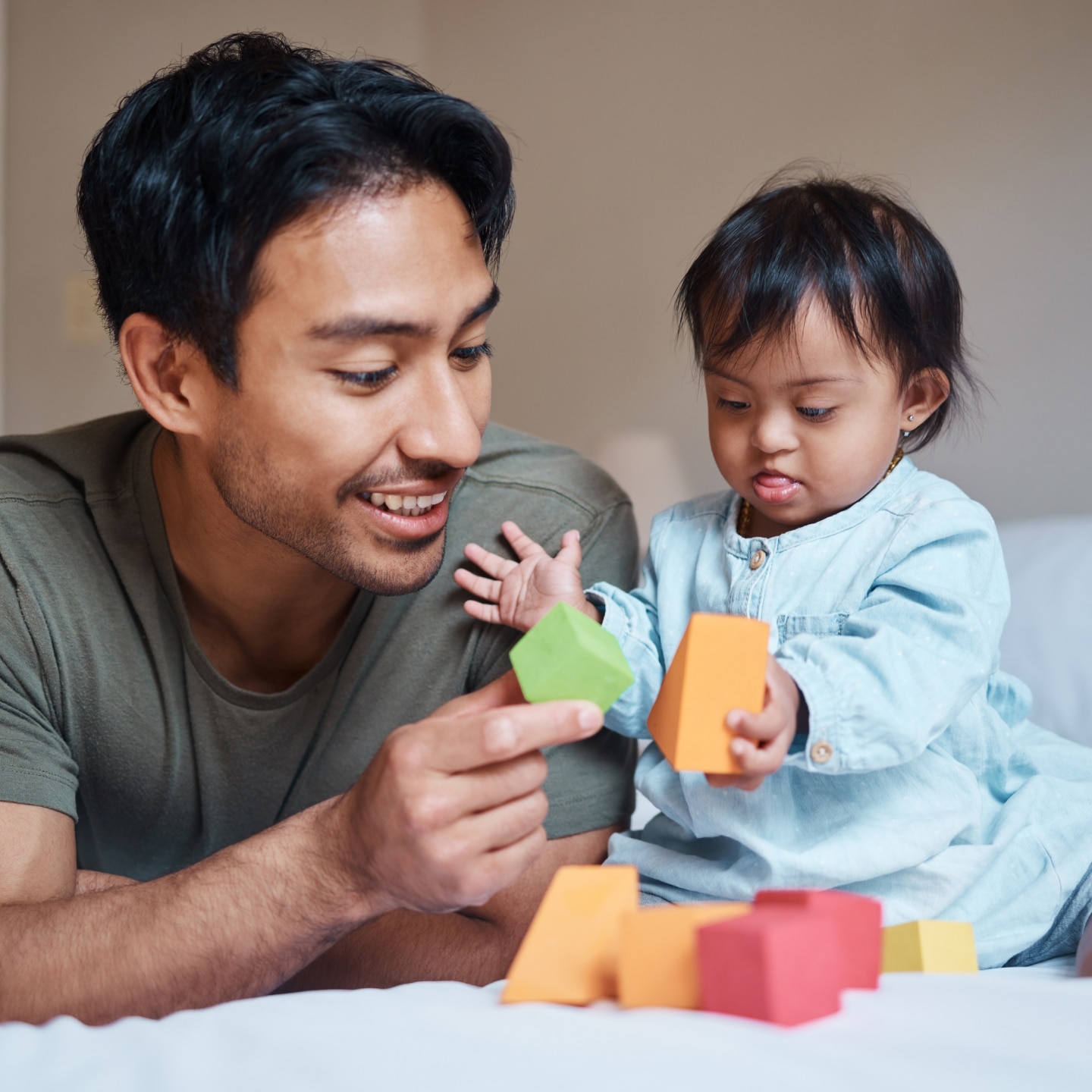 Baby, down syndrome and learning on a bed with child and father playing