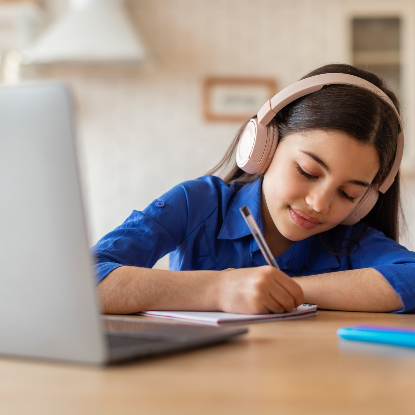 Schooler girl doing homework at laptop taking notes at home