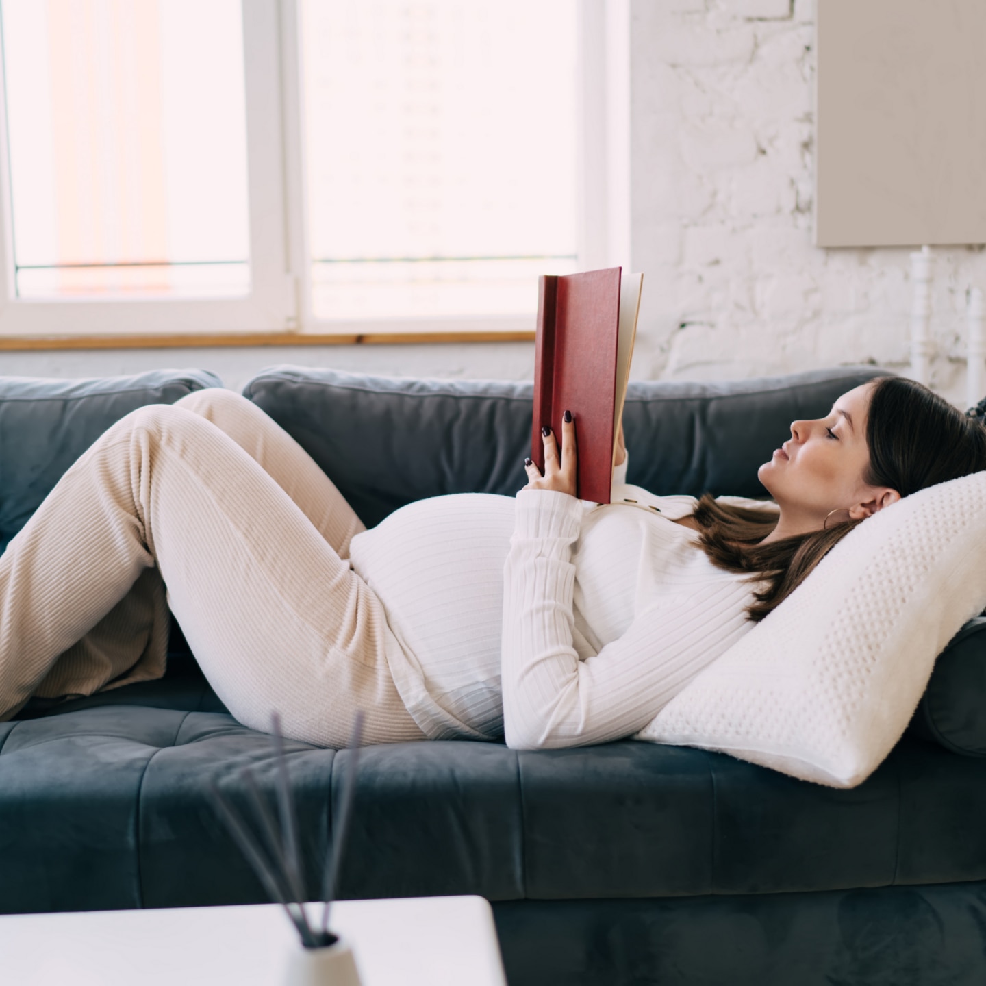 Schwangere liest ein Buch auf der Couch