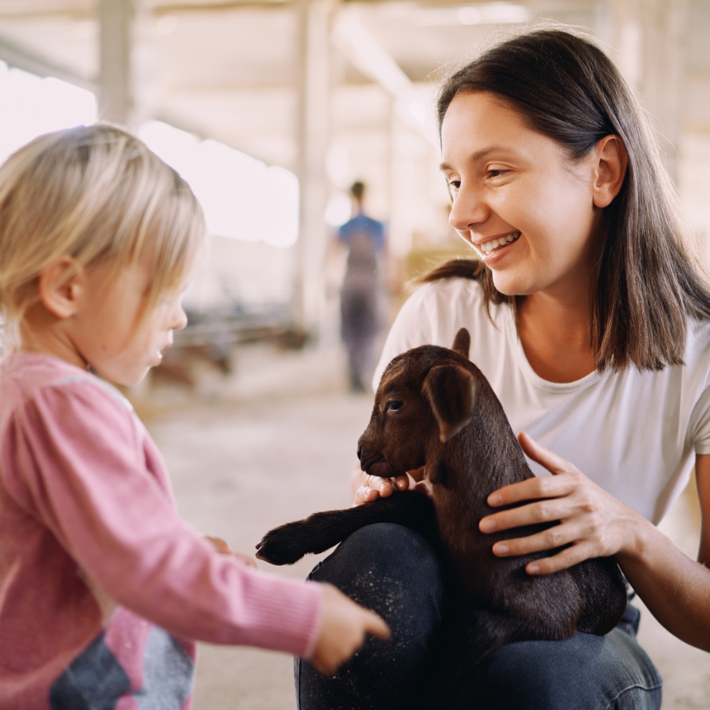 Little girl touches with her fingers a goatling in her mother arms on a farm
