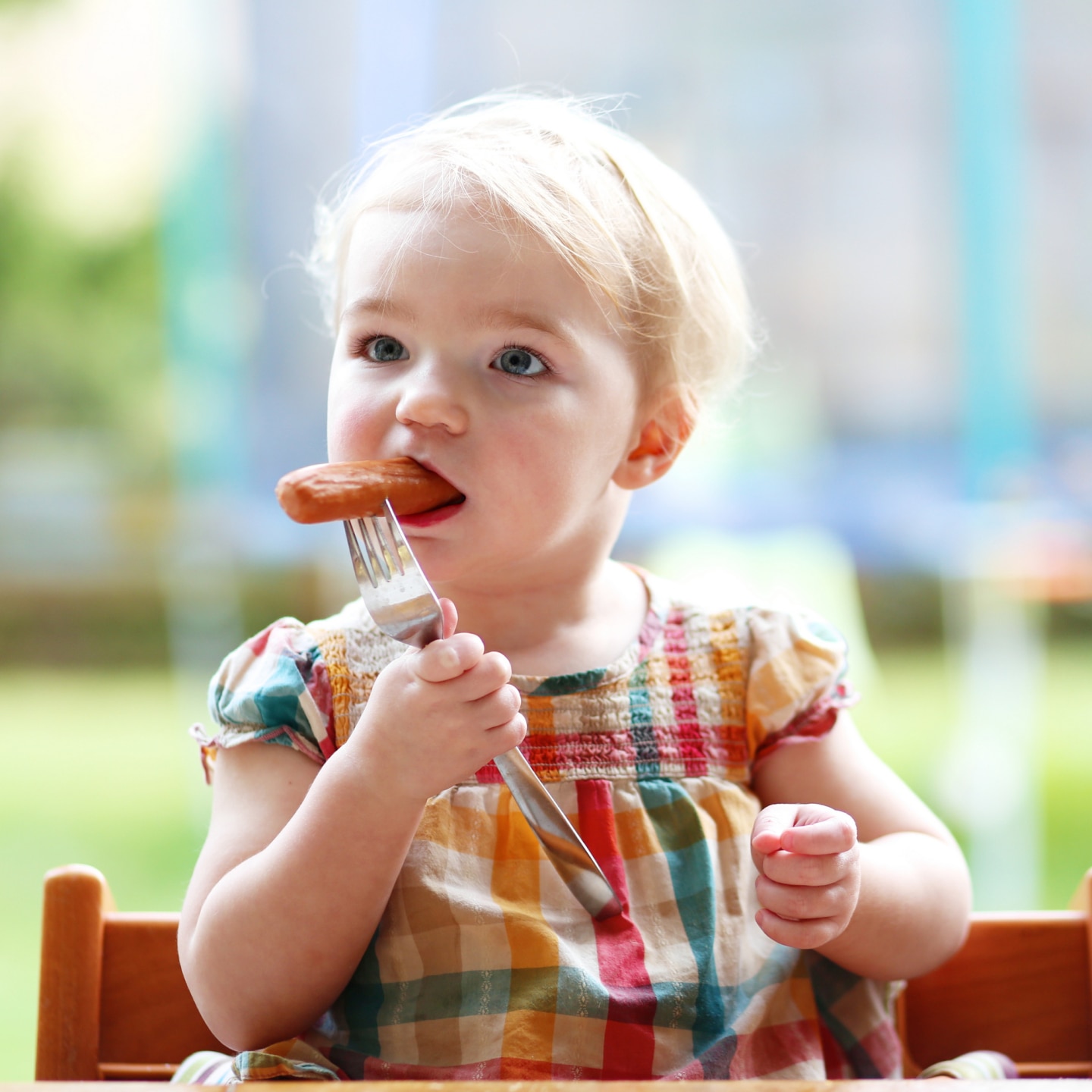 Cute baby girl eating sausage from fork
