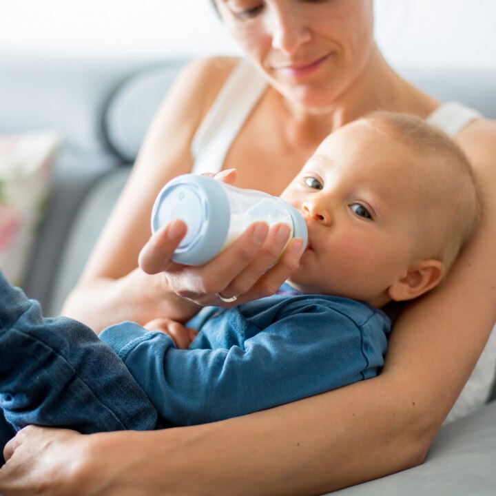 Mother, feeding her baby boy from bottle, sitting on the couch at home