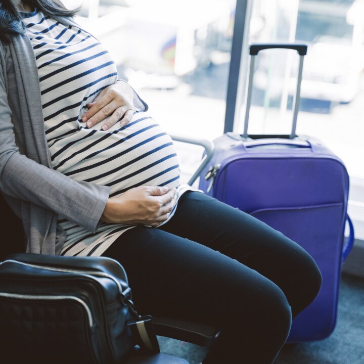 pregnant woman sitting beside a suitcase on the airport