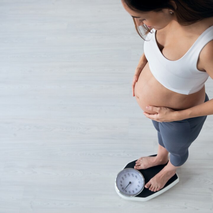 Pretty young pregnant woman standing on scales at home