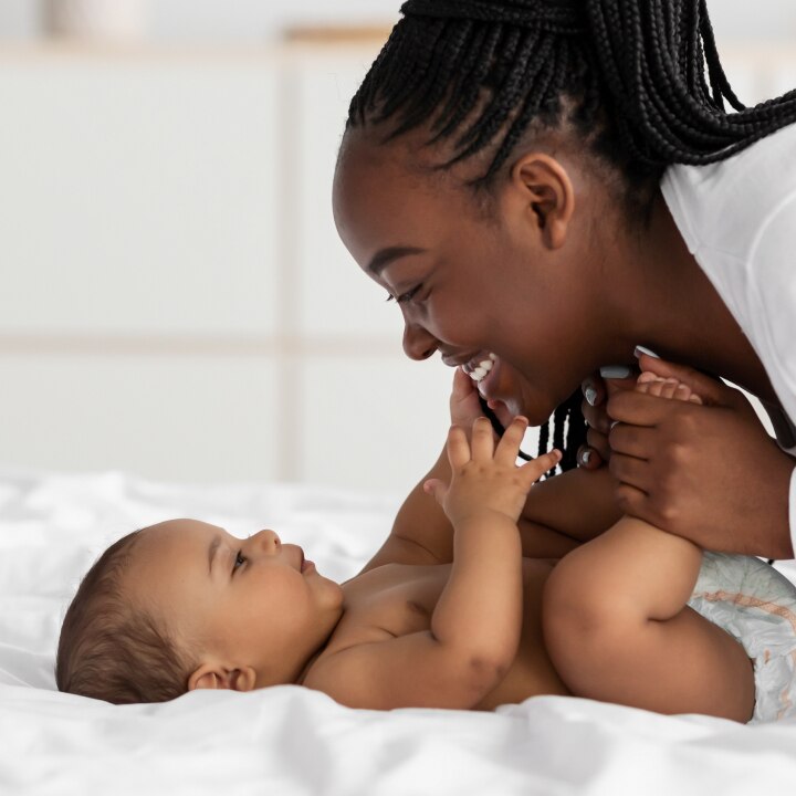 African American mom playing in bed with her black baby